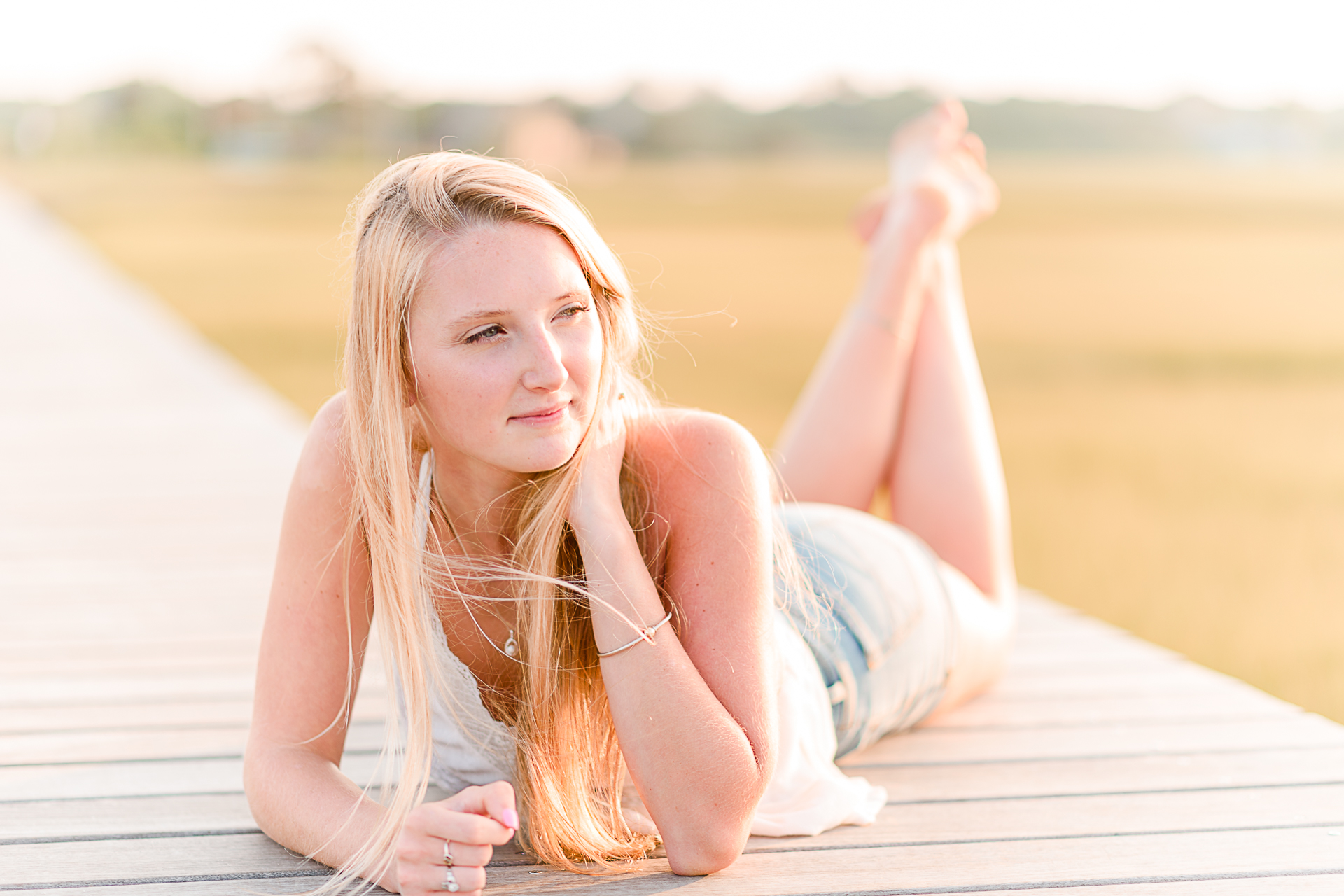 Photo by Cape Cod Senior Portrait Photographer Christina Runnals | High school senior girl laying on her stomach on a boardwalk looking away from the camera