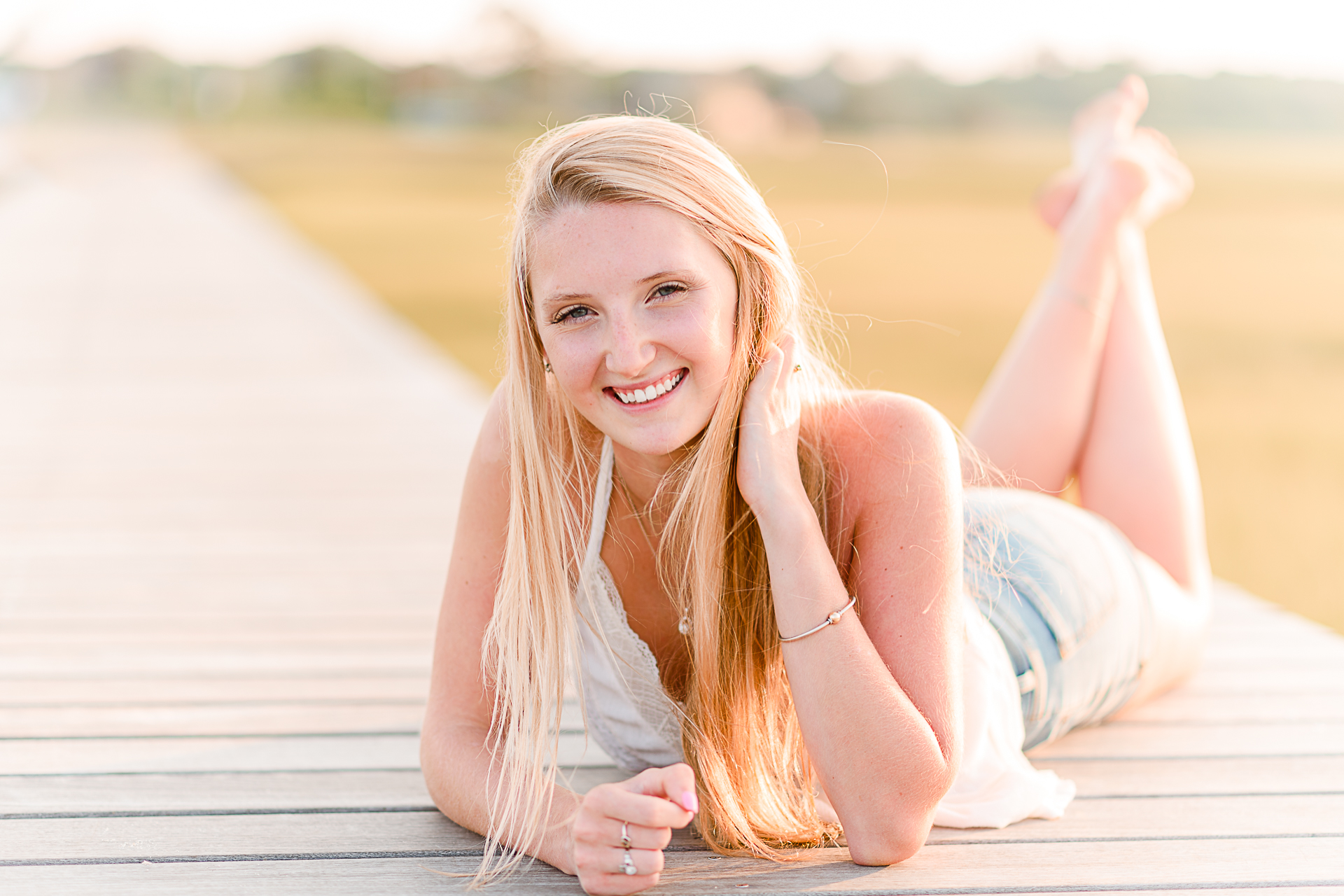 Photo by Cape Cod Senior Portrait Photographer Christina Runnals | High school senior girl laying on her stomach on a boardwalk smiling at the camera