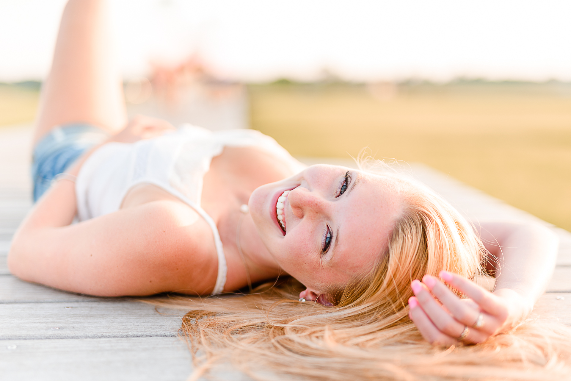 Photo by Cape Cod Senior Portrait Photographer Christina Runnals | High school senior girl laying on her back on a boardwalk smiling at the camera