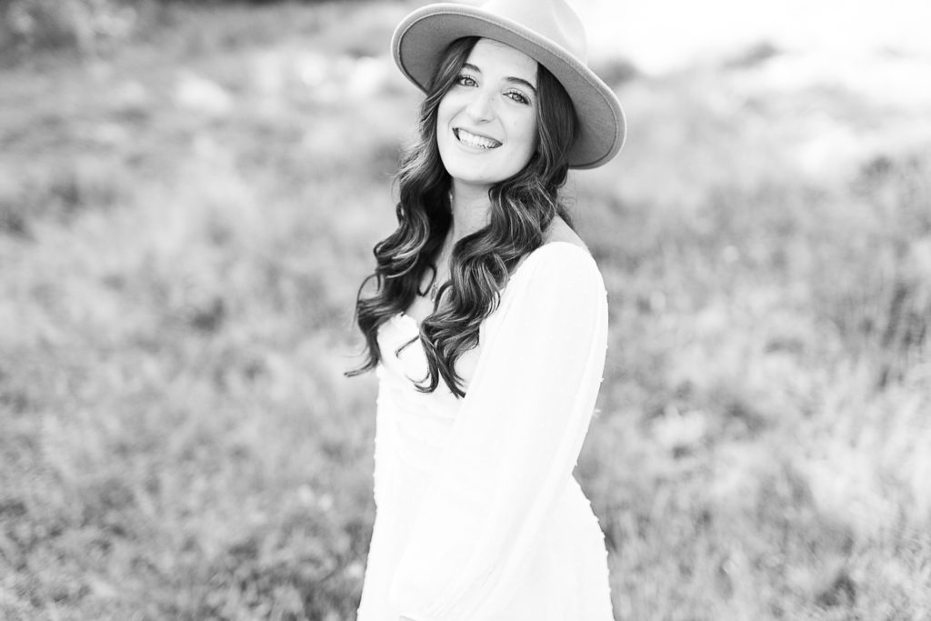 Black and white photo taken by Massachusetts senior photographer Christina Runnals | High school senior girl wearing a hat in a field