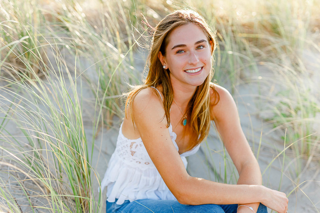 Cohasset Sandy Beach Senior Pictures by Christina Runnals | A high school senior girl sitting in beach grass smiling