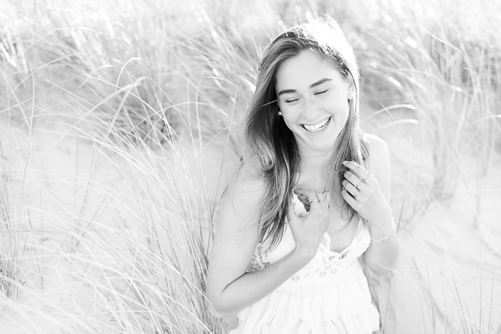 Cohasset Sandy Beach Senior Pictures by Cohasset photographer Christina Runnals | A high school senior girl sitting in beach grass laughing