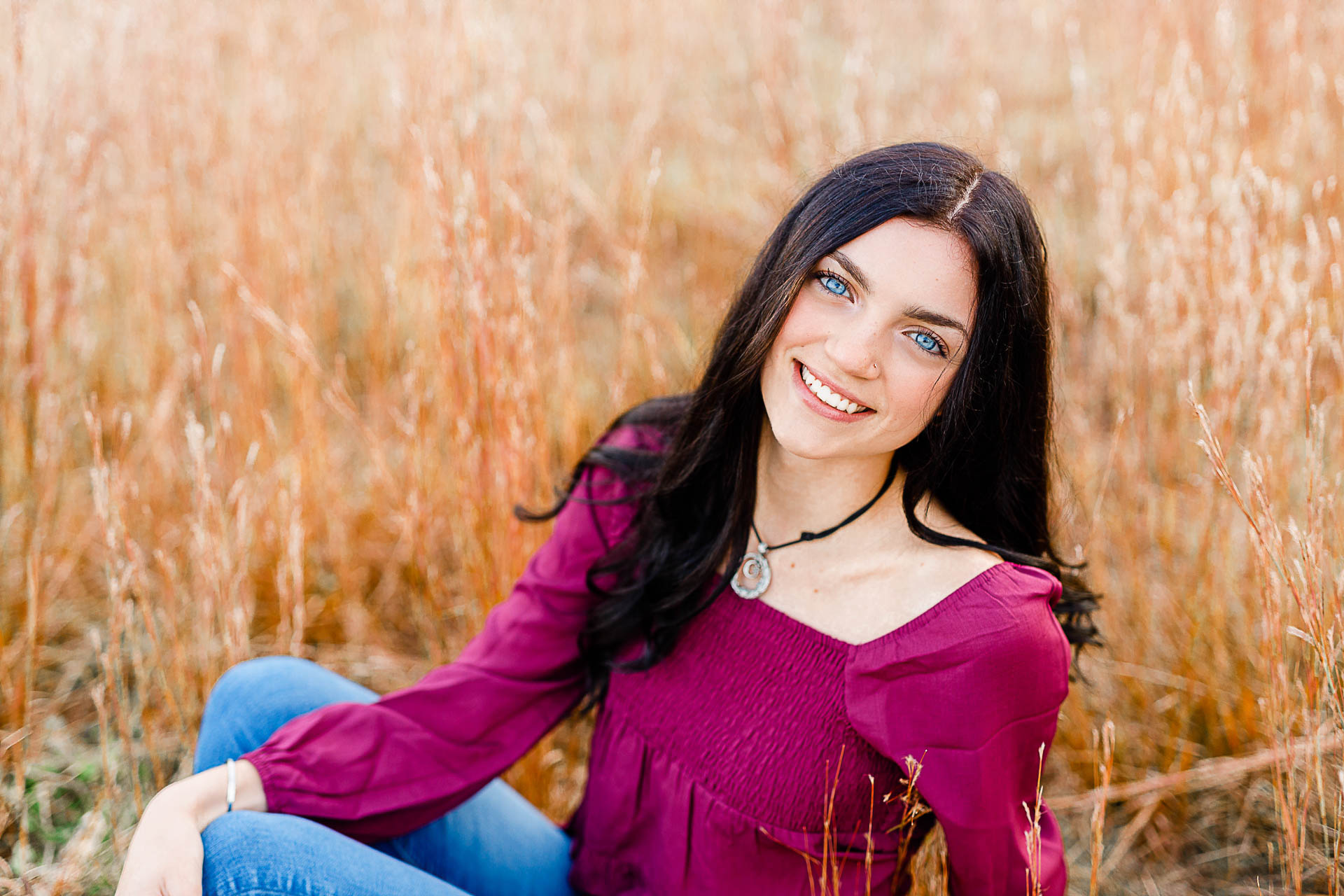 Photo by Duxbury senior photographer Christina Runnals | A high school senior girl with big blue eyes sitting in a field smiling