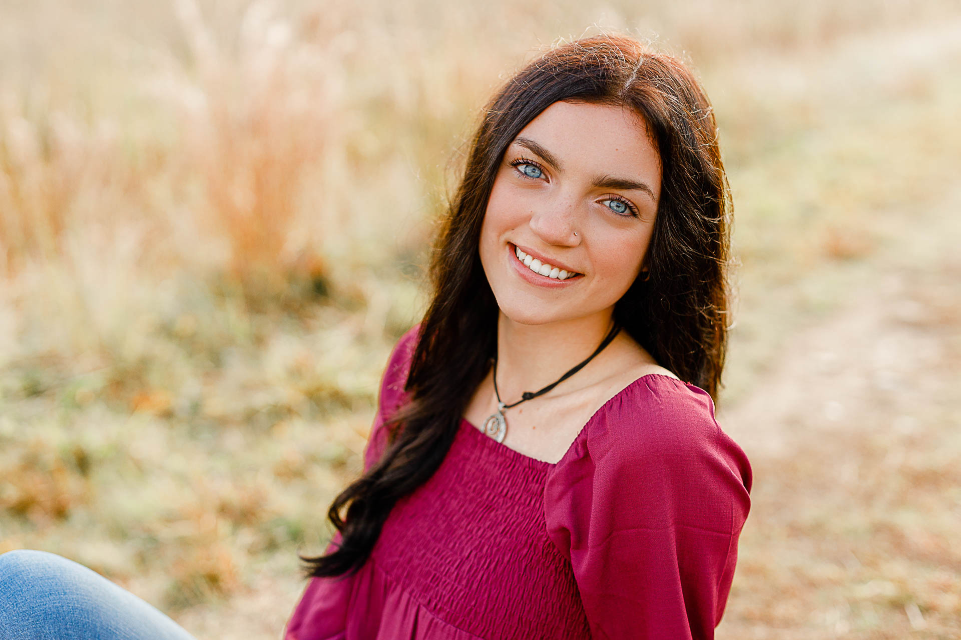 Photo by Duxbury senior photographer Christina Runnals | A high school senior girl with big blue eyes sitting in a field smiling
