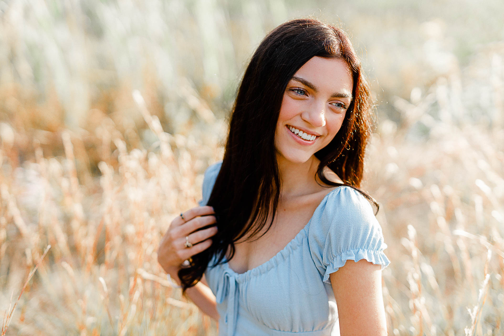 Photo by Duxbury senior photographer Christina Runnals | A high school senior girl with big blue eyes laughing and sitting in a golden field