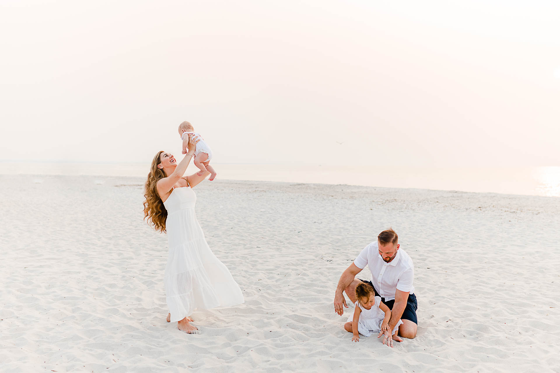 Photo by Cape Cod Family Photographer Christina Runnals | Mom spinning baby and dad playing in sand with daughter on beach