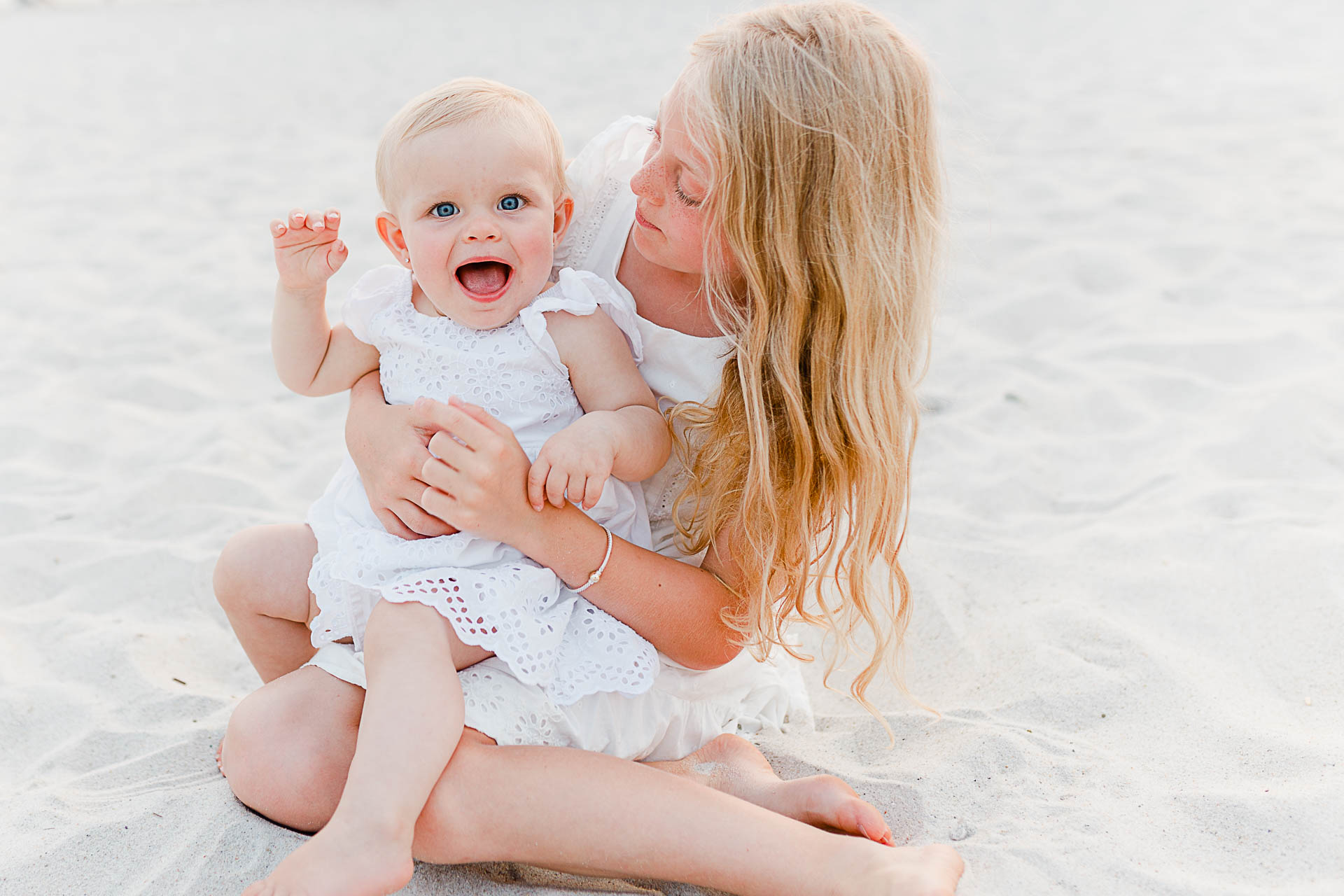Photo by Cape Cod Family Photographer Christina Runnals | Big sister holding baby sister on beach wearing white