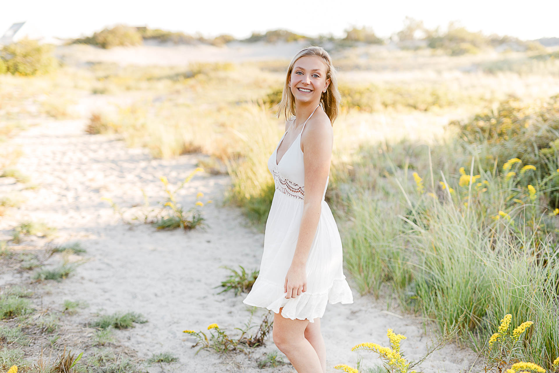 Photo by Christina Runnals Photography who specializes in luxe senior portraits | Girl standing in beach grass twirling a white dress