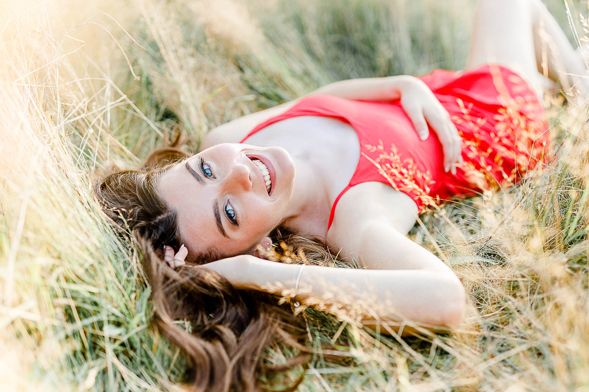 Photo by Duxbury senior portrait photographer Christina Runnals | High school senior girl wearing a red dress and laying in a field | Hot senior pictures
