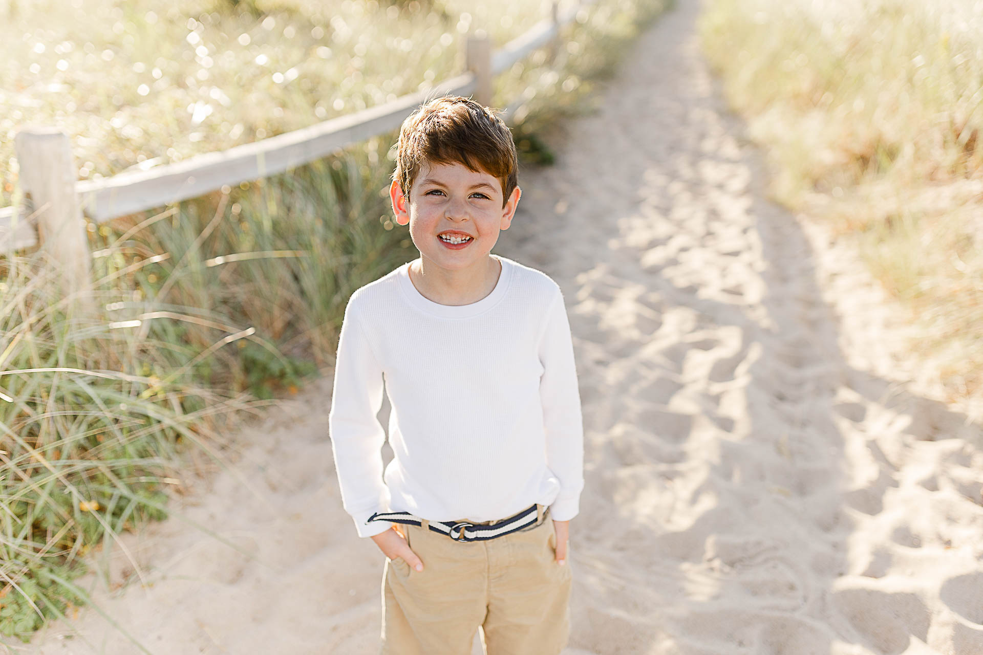 Watch Hill Family Portraits by Christina Runnals Photography | Boy standing in sand near fence and beach grass