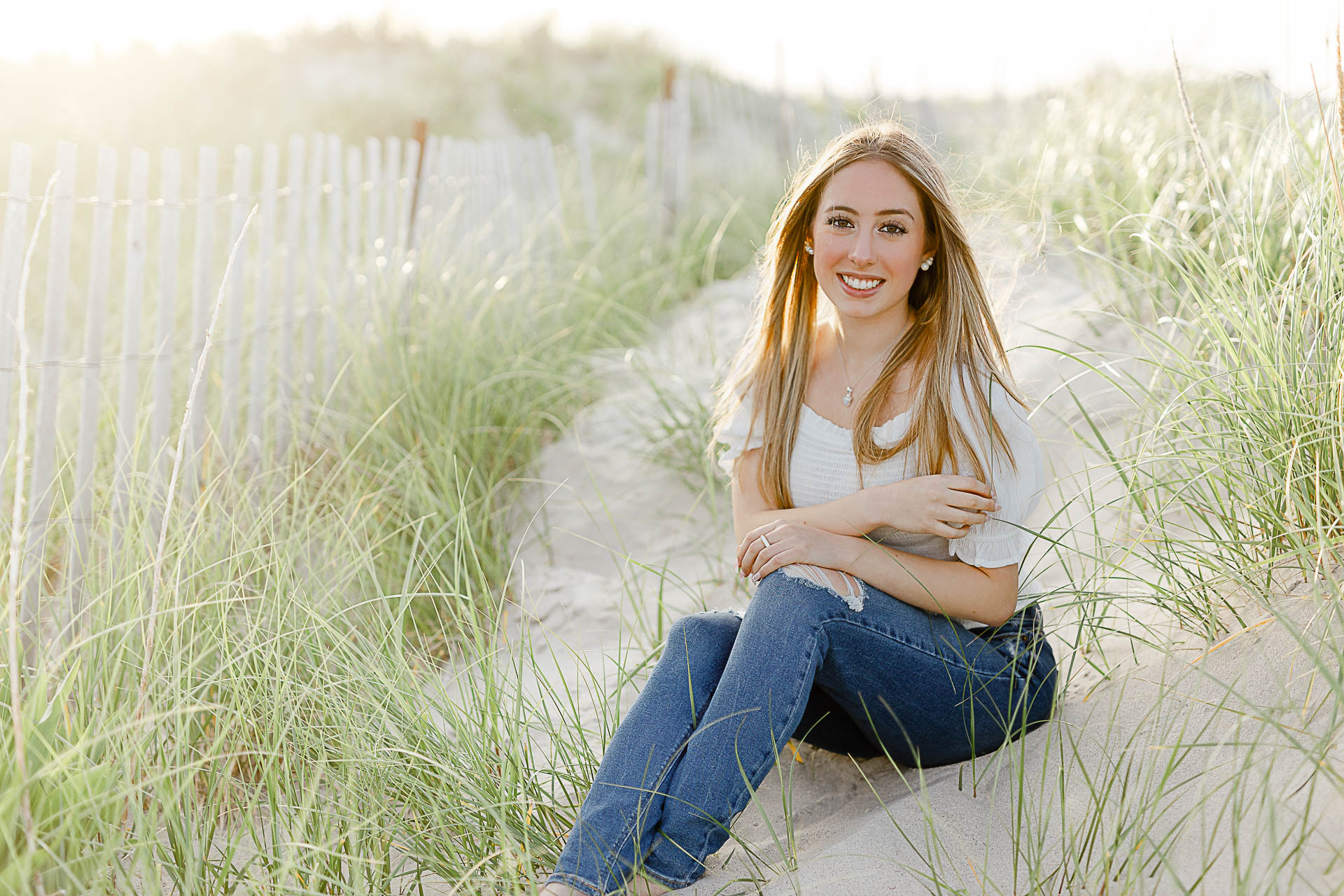 Photo by Arlington senior portrait photographer Christina Runnals | Girl sitting in beach grass with a fence