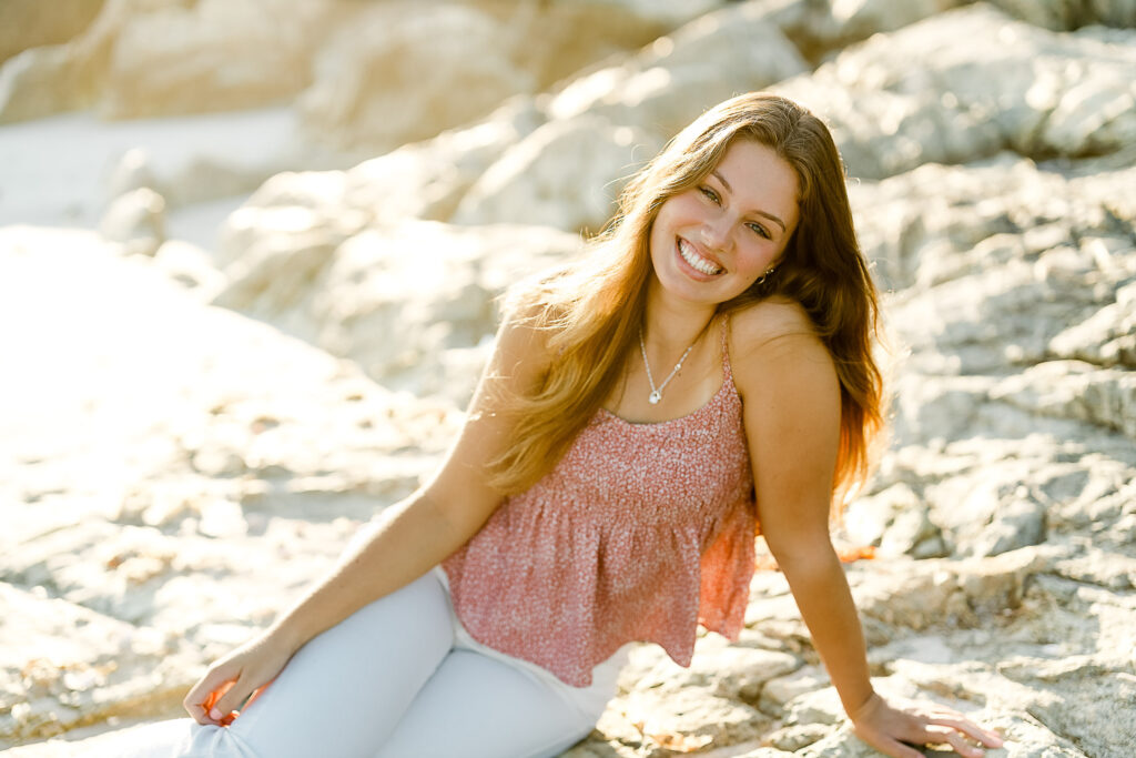 Senior pictures at sunrise are stunning in New England | Image by Christina Runnals Photography | Girl sitting on rocks in pink floral tank top