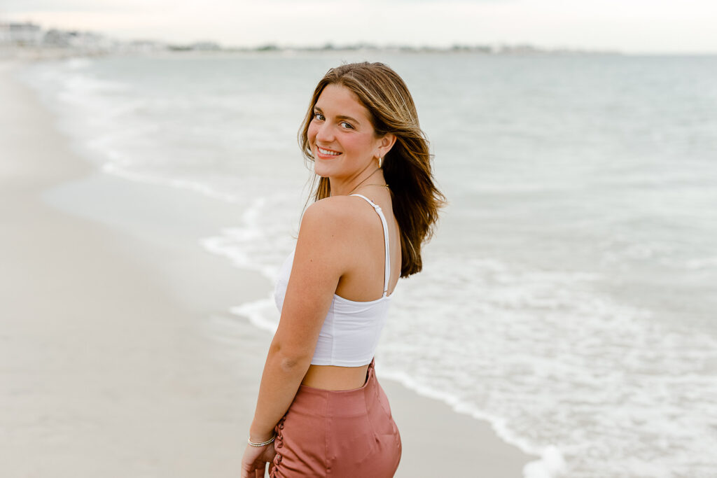 This image demonstrates that when choosing outfits for your senior photos it is best to select a variety of looks such as Annabelle's dressy look at the beach in a silk rust colored skirt and white tank top.