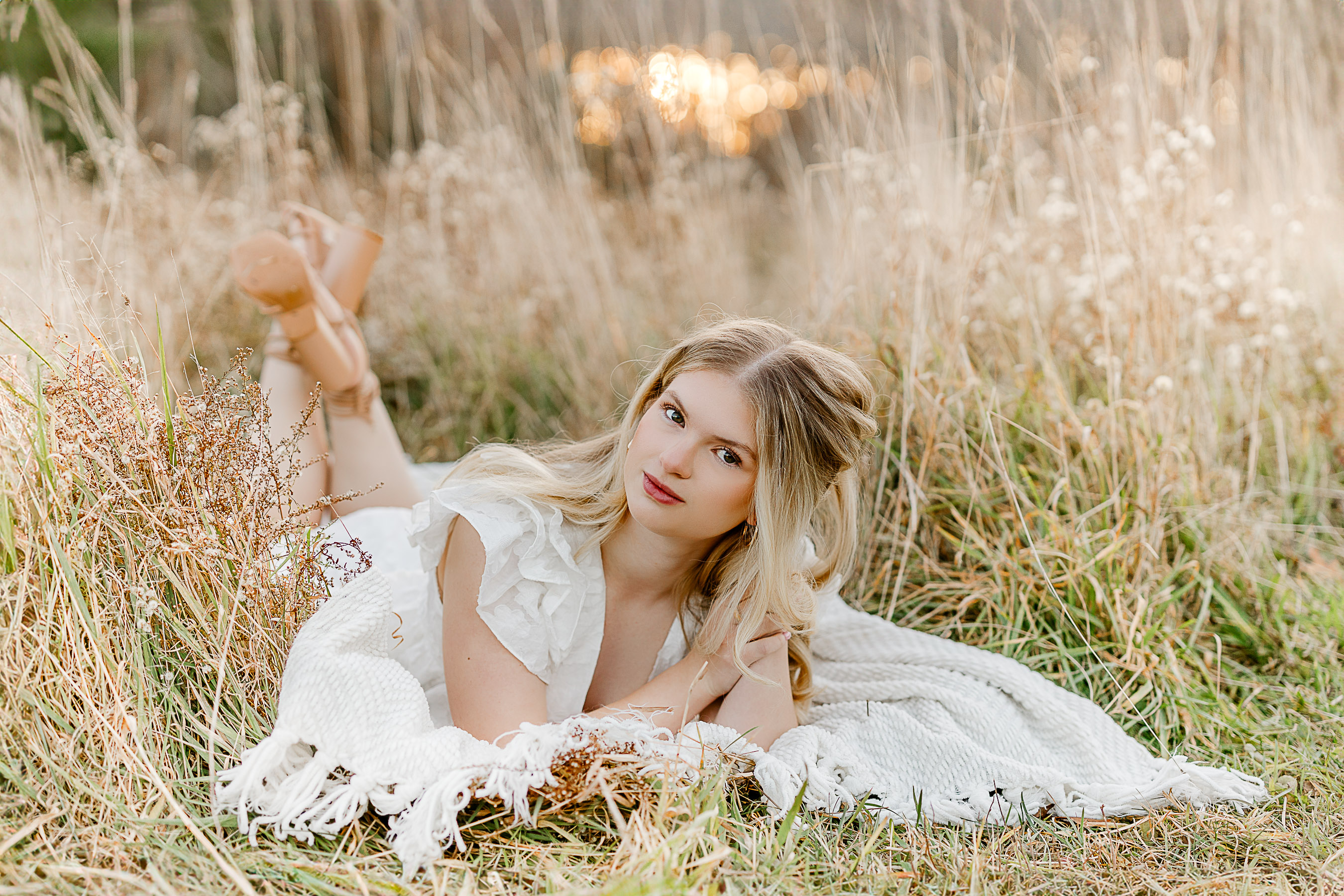 This image demonstrates that when choosing outfits for your senior photos it is best to select neutral colors, such as Lauren's cream colored dress while laying in a field of gold