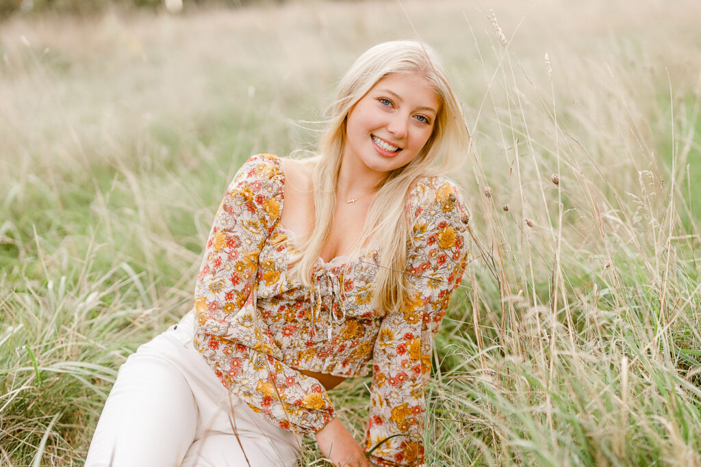 Fall senior pictures in Massachusetts featuring Elizabeth in cream colored pants, a floral top, and long blonde hair.
