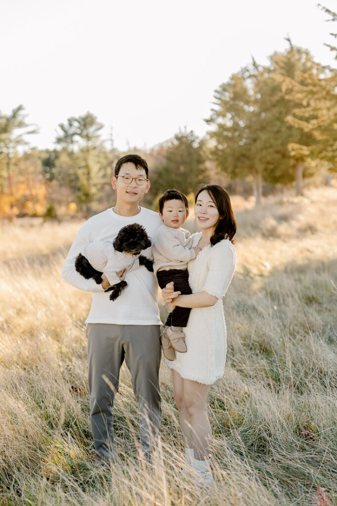 Newton MA family photography featuring a mom, dad, and their little boy in a beautiful field of tall grasses and pine trees