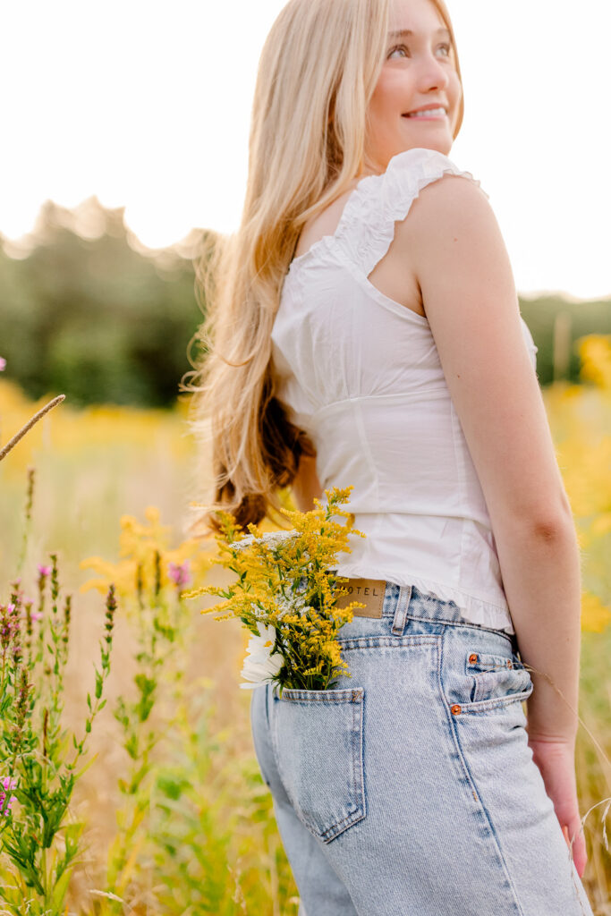 Massachusetts senior photos with yellow wildflowers and a girl wearing jeans and a white shirt with a bouquet of flowers in her back pocket