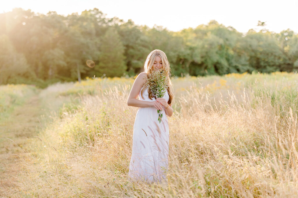 Massachusetts senior photos with wildflowers and a girl wearing a long white dress smelling flowers