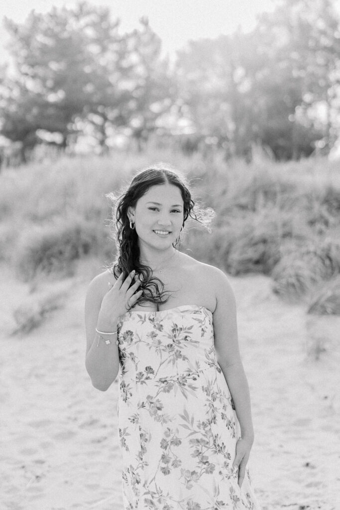 Lexington MA senior pictures taken on the South Shore at a beach.  Featuring a senior with long curly dark brown hair in a long white dress with a blue floral pattern.