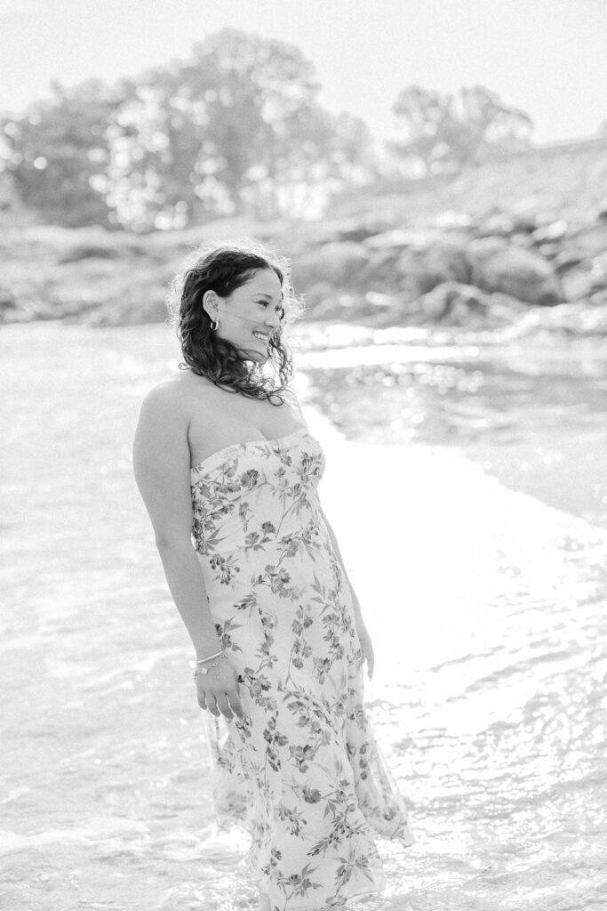 Lexington MA senior pictures taken on the South Shore at a beach.  Featuring a senior with long curly dark brown hair in a long white dress with a blue floral pattern.